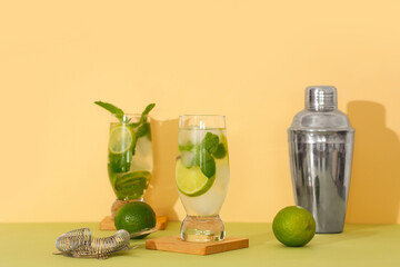 Glasses of fresh mojito with bartender equipment on green table against beige background