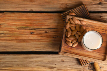 Glass of fresh almond milk and board with nuts on wooden background