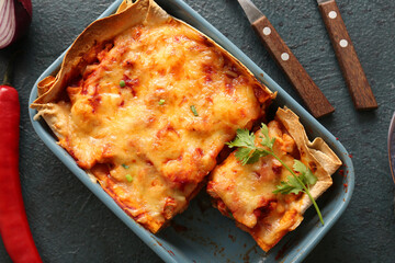 Baking dish with tasty enchilada on dark color background, closeup