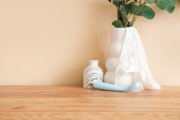 Vibrator with panties and vases on table near beige wall