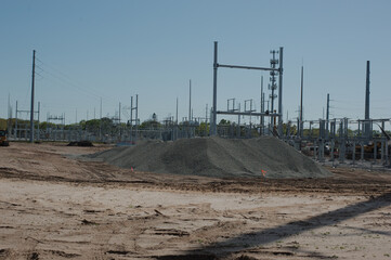 Substation during its construction phase with exposed metal framework, gravel ground, and electrical infrastructure components visible. Part of an electrical grid that transforms voltage from high to 