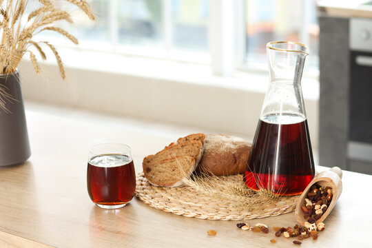 Jug and glass of tasty kvass with bread slices and spikelets on table in kitchen