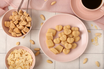 Plates with tasty marzipan candies, almond flakes and cane sugar on light tile background