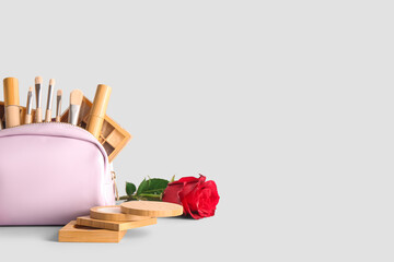 Cosmetic bag with makeup products and red rose on grey background. Valentine's day celebration