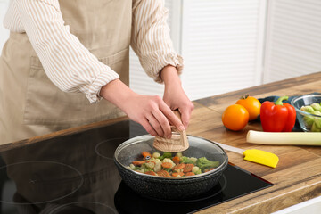 Young woman frying tasty vegetables in kitchen