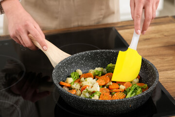 Young woman frying tasty vegetables in kitchen