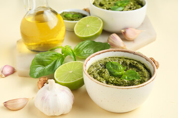 Bowls with delicious pesto sauce, ingredients and jug of oil on beige background