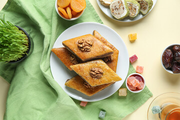 Tasty baklava, traditional sweets and green wheat grass on yellow background. Nowruz Bayram celebration