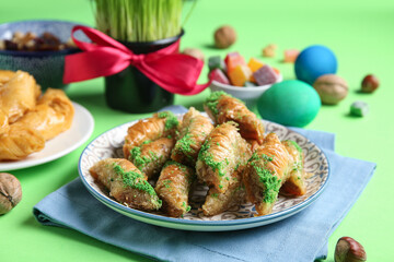 Tasty baklava, wheat grass and traditional sweets on green background, closeup. Nowruz Bayram celebration