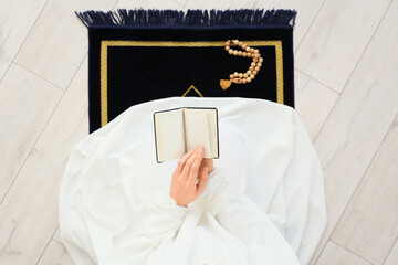 Muslim woman with Koran praying on prayer carpet at home, top view. Ramadan celebration