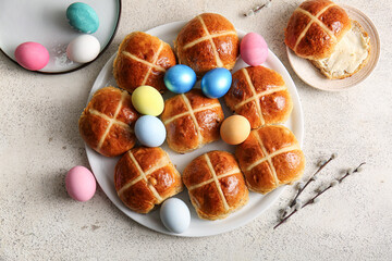 Plates with Easter cross buns, eggs and willow branches on white grunge background
