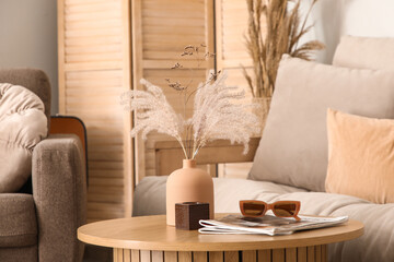 Vase with dry reeds, sunglasses and magazines on table in living room