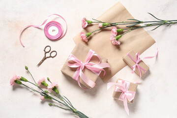 Gift boxes with pink carnations, wrapping paper and scissors on beige grunge background. International Women's Day