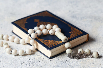 Koran with tasbih on white grunge background, closeup. Ramadan celebration