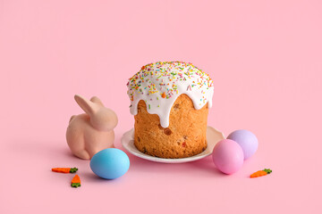 Plate with sweet Easter cake, painted eggs and toy bunny on pink background