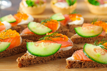 Tasty canapes with salmon and cucumber on wooden board, closeup
