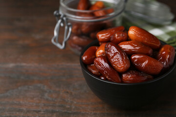 Tasty dried dates in bowl and jar on wooden table, closeup. Space for text