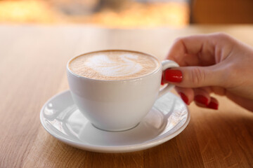 Woman with cup of aromatic coffee at wooden table in cafe, closeup