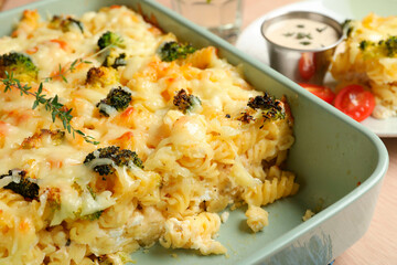 Tasty pasta casserole with cheese and broccoli in baking dish on wooden table, closeup
