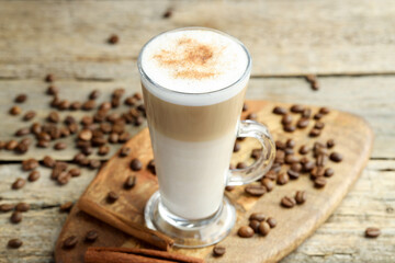 Tasty latte macchiato in glass cup, coffee beans and cinnamon on wooden table, closeup