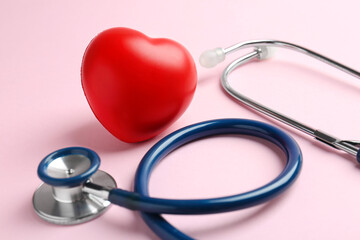 Cardiology. Stethoscope and red decorative heart on pale pink background, closeup