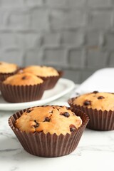 Delicious muffin with chocolate chips on white marble table, closeup