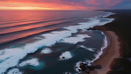 A sunset over the coast, observed from above, with waves crashing and the horizon stretching out
