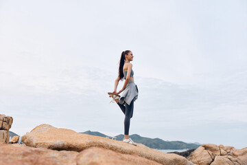Naklejka premium Young woman practicing yoga on rocky terrain, showcasing strength and flexibility in sporty attire, embodying a healthy lifestyle and tranquility