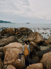Solo female adventurer exploring rocky coastline during overcast day, showcasing determination and...