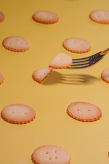黄色背景に規則正しく並んだビスケットをフォークで持ち上げている