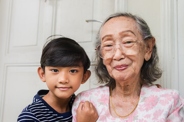 Happy Southeast Asian grandmother smiling and posing together with her grandson during visit at...