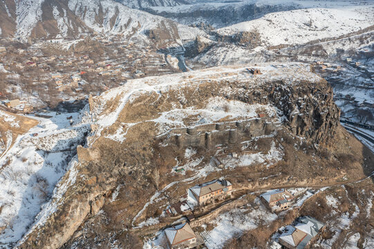 Aerial drone view of Bjni village in Kotayk, Armenia, featuring the historic Bjni Fortress, snow-covered village houses, winding streets, and the Hrazdan River flowing through the winter landscape