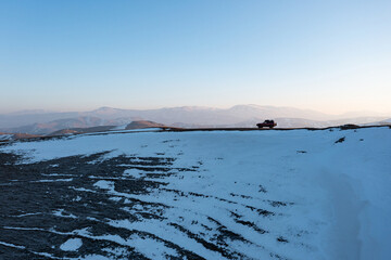 Aerial drone view of a red American 4x4 off-road SUV on a snowy mountain ridge between the mountains of Lori and Tavush provinces, Armenia. Perfect scene for adventure travel and off-road exploration © Hrach