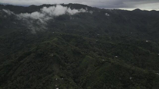 Drone orbits high over cacao plantations and small villages spread throughout green valley on cloudy afternoon in Semuc Champey, Guatemala
