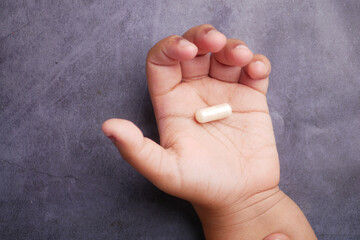 Child's hand holding a dietary supplement capsule in natural light