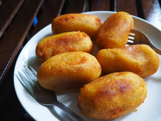 Fried sweet potato with golden brown color with crispy exterior and soft and sweet filling is beautifully served on a white plate, signifying a delicious and comforting snack or dessert.