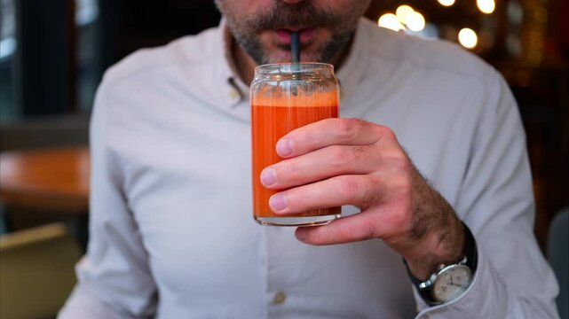 Close up of a man drinking an orange and carrot juice in a glass with a black straw