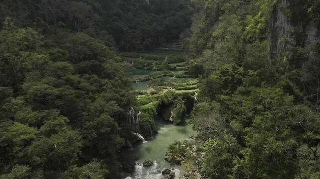 Drone slowly orbits over entrance to underground river below limestone pools on the Cahabon River in Semuc Champey, Guatemala
