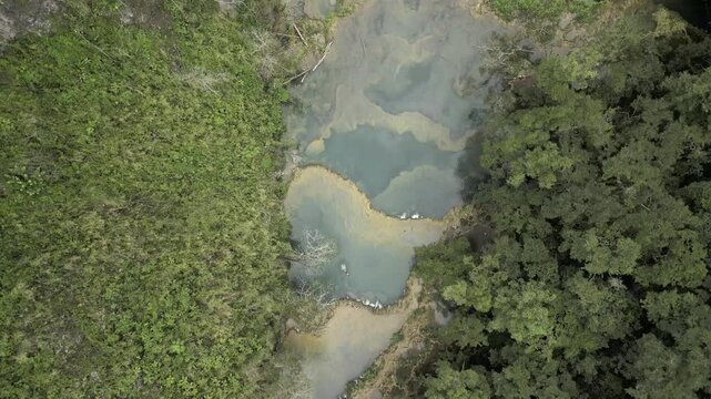 Drone flies high over reflective limestone pools and rapids in Cahabon River on a sunny day in Semuc Champey, Guatemala