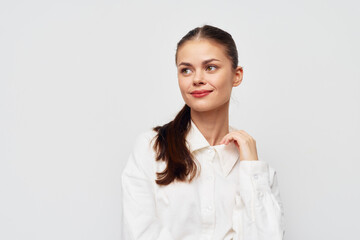 Fototapeta premium Young woman with a cheerful expression, wearing a white shirt against a plain light background, exuding confidence and positivity Her hairstyle is a simple ponytail