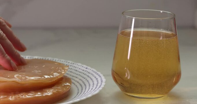 A hand is carefully preparing the SCOBY culture for brewing delicious kombucha next to a glass of refreshing tea