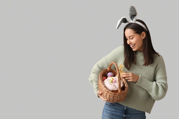 Pretty young woman with bunny ears and Easter basket on grey background