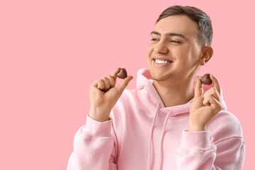 Young man with heart-shaped chocolate candies on pink background