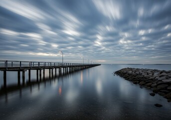 Obraz premium Long Exposure Pier with Moody Sky Over Calm Water Landscape