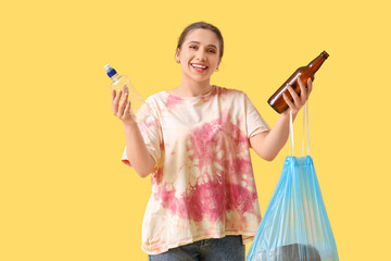 Young woman with bottles and garbage bag on yellow background. Waste sorting concept