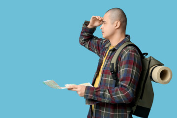 Young male tourist with map and backpack on blue background