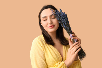 Beautiful young woman with bouquet of lavender flowers on beige background