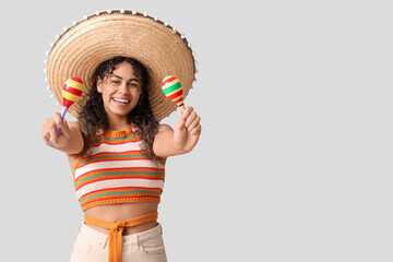 Happy young African-American woman in sombrero hat with maracas on grey background