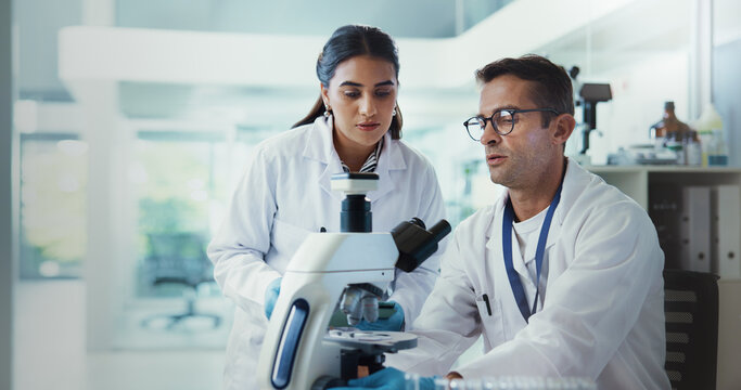 Scientist, people and microscope in lab for advice, testing and medical research. Pathology, man and science assistant with mentor report for pharmaceutical or biotech experiment for breakthrough