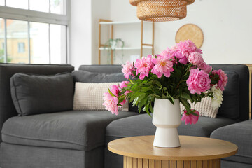 Beautiful pink peony flowers in vase on coffee table near cozy sofa in interior of living room